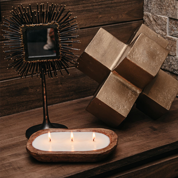 Candle holder with three candles, decorative mirror, and geometric sculpture on a wooden surface.